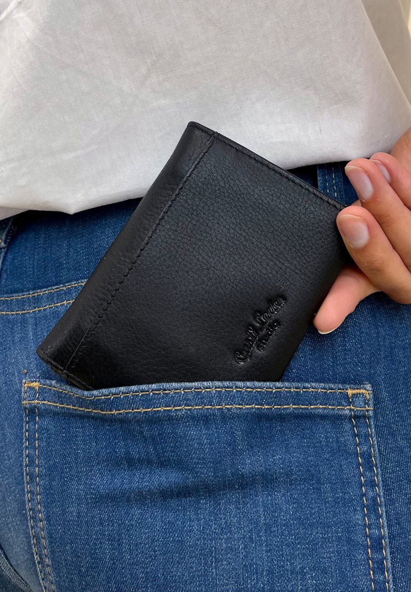 Mano che inserisce un portafoglio in pelle nera nella tasca posteriore di jeans di denim blu su sfondo di una camicia bianca.