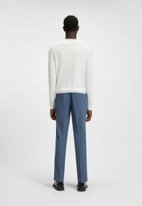 Maglietta bianca a maniche lunghe abbinata a pantaloni su misura blu. Design slim fit con texture liscia. Scarpe nere completano l'outfit.