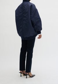 Granatowa bomberka z elastycznymi mankietami i dołem, połączona z ciemnymi dżinsami i czarnymi klapkami na obcasie. Miękka faktura, oversize'owy krój.