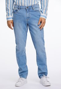 Vaqueros de mezclilla de un azul claro con corte recto, con cremallera y cinco bolsillos. Combinados con zapatillas blancas y una camisa a rayas azules.