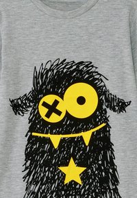 Graues T-Shirt mit einem schwarzen, zotteligen Monster-Design, das gelbe Augen und einen gefräßigen Mund hat, akzentuiert mit einem gelben Stern und dreieckigen Zähnen.