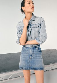 Lyseblå denimjakke med lange ærmer og brystlommer, kombineret med en lys blå denim mininederdel, begge med subtil falmning.