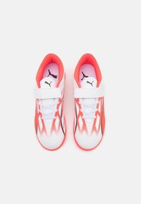 Zapatillas deportivas Puma con una parte superior blanca con detalles rojos, una correa de velcro, acentos negros y una textura suave.
