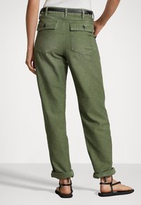 Groene katoenen broek met een relaxte pasvorm, voorzien van twee achterzakken, opgerolde manchetten en een zwarte riem. De stof heeft een gestructureerde afwerking.