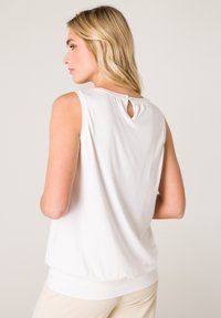 White sleeveless top with a keyhole detail at the back, made of soft fabric, featuring a relaxed fit and gathered hem at the waist.