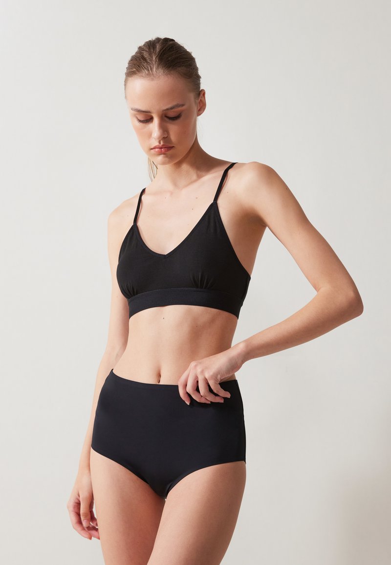 Svart bralette med V-hals og tynne stropper, sammen med høyt liv svarte truser. Glatt tekstur og minimalistisk design.