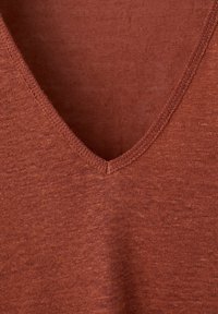 Tissu tricoté couleur rouille avec un col en V et des coutures visibles le long du bord.