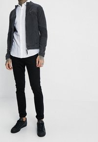 Szara teksturowana kurtka z zamykaną na zamek kieszenią, czarne dopasowane spodnie i czarne trampki. Pod spodem biała koszula, szczegółowo przeszyte ramiona.