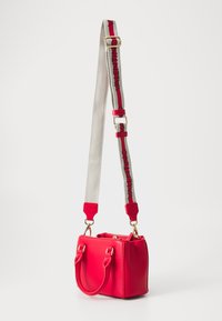 Spilgti sarkans roku darbs ar kvadrātu formu, gluda āda, divi īsie rokturi un noņemama pelēka siksna ar sarkaniem un melniem zīmoliem. Zelta aksesuāri.