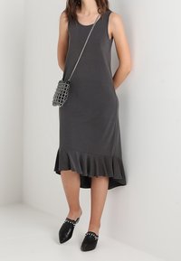 Szara sukienka bez rękawów z falbaniastym dołem, wykonana z miękkiego materiału. W połączeniu z czarnymi klapkami z ćwiekami i małą metaliczną torebką.