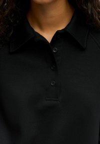 Schwarzes Poloshirt mit klassischem Kragen, fünf Knöpfen und glatter Textur mit einem subtilen Glanz. Geeignet für legere oder semi-formelle Anlässe.