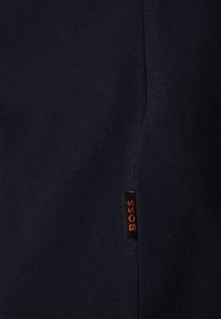 Marinblått bomullstyg med en slät yta; har en orange "BOSS"-etikett vid sidosömmen. Enkel design utan mönster eller accenter.