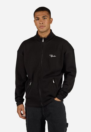 Casaco preto com textura canelada, com fecho éclair e colarinho alto, bolsos laterais com fecho e logótipo branco no peito. Textura robusta com um corte descontraído.