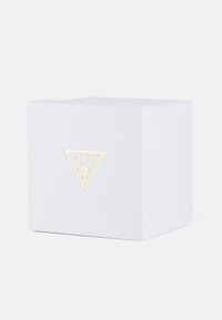 Biały teksturowany box z trójkątnym złotym logo oraz słowem "GUESS" i znakiem zapytania pośrodku.