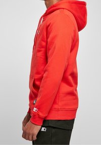Sudadera con capucha roja hecha de una mezcla de algodón, con un bolsillo canguro, capucha ajustable y parches de logo en la manga y el cuerpo.