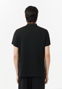 Svart polo skjorta med krage och korta ärmar, med vinröda accenter längs axlarna; enkel, texturerad tyg.