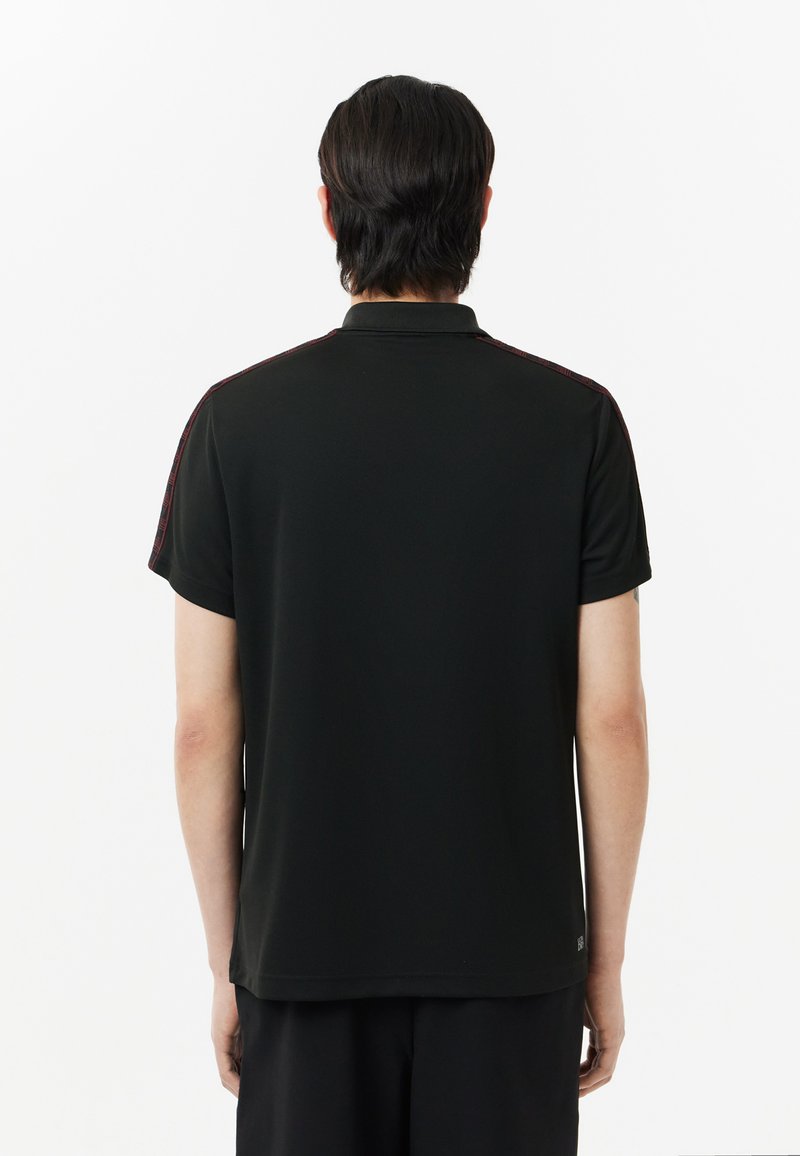 Schwarzes Poloshirt mit Kragen und kurzen Ärmeln, das bordeauxfarbene Akzente an den Schultern aufweist; einfacher, strukturierter Stoff.