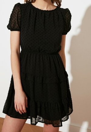 Vestido negro en capas hecho de tela transparente con lunares texturizados, mangas cortas con volantes y una cintura elástica para un ajuste relajado.