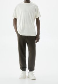 Vit bomull t-shirt i kombination med mörkgröna joggerbyxor; modellen bär vita sneakers med grå detaljer; avslappnad passform, minimalistisk design.