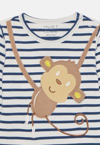 Gestreiftes Langarmshirt in Marineblau und Weiß, mit einem braunen Affenapplikation und gelben Ohrakzenten sowie gestickten Details auf der Vorderseite.
