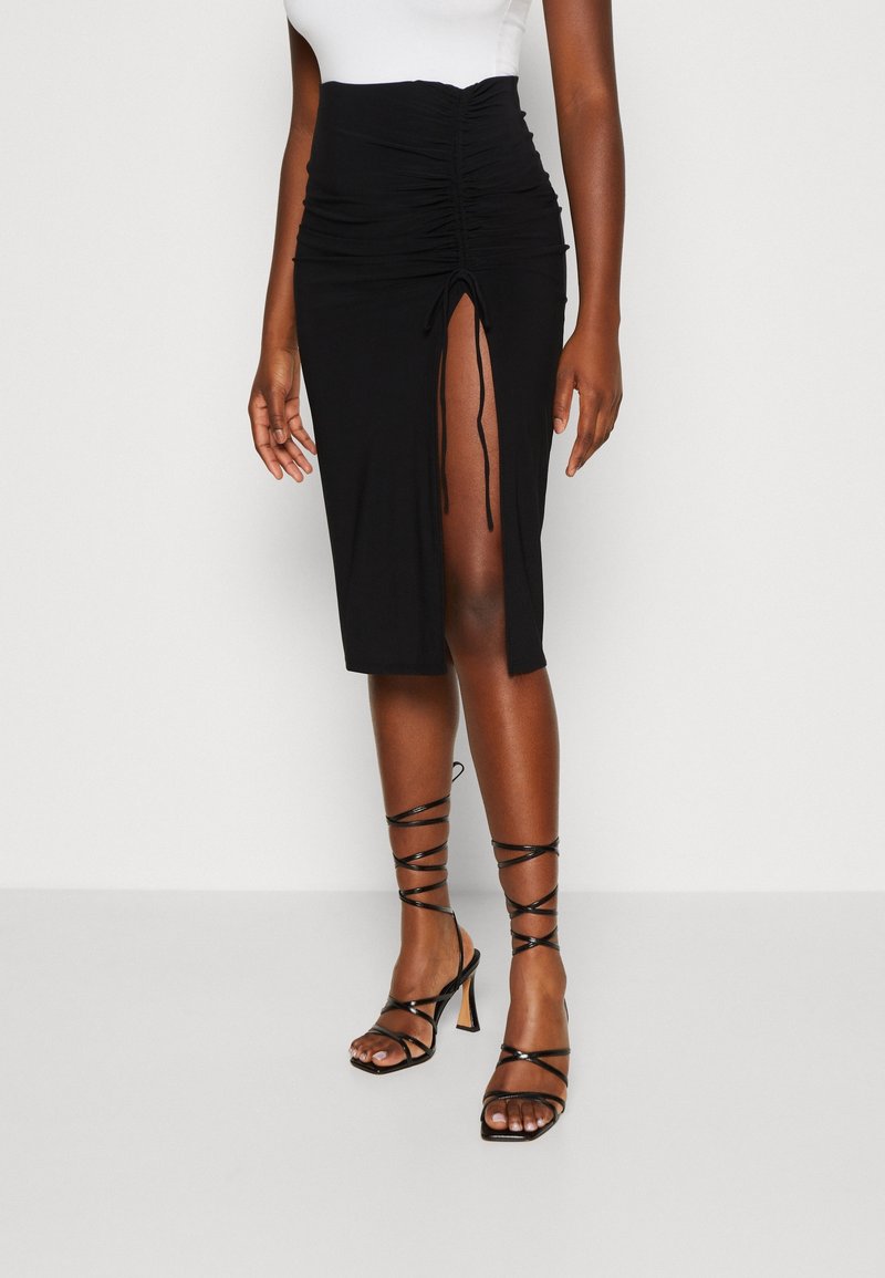 Svart midiskjol med samlad textur och framfickor, i kombination med svarta klackar med remmar. Kjolen har dragsko-detaljer på sidan.