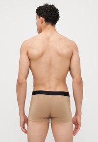 Beige boxeralsók fekete derékrészsel, puha tapintással és testhezálló fazonnal, hátulról láthatók egy mezítelen torzón.