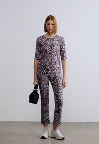 Σετ τοπ και κολάν με σχέδιο λεοπάρ σε αποχρώσεις καφέ και μαύρου, συνδυασμένο με λευκά αθλητικά παπούτσια και μικρή μαύρη τσάντα. Λείο, εφαρμοστό ύφασμα.