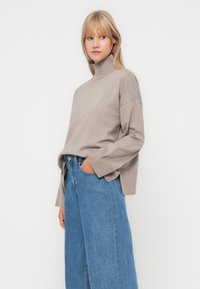 Beige turtleneck sweater with ribbed texture and side slits, paired with high-waisted, wide-leg blue jeans. Simple and relaxed fit.