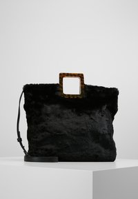 Svart faux fur-handväska med en texturerad yta, fyrkantigt sköldpaddsblockhandtag och en justerbar svart axelrem för mångsidiga bäralternativ.