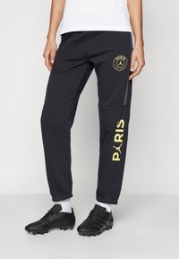 Czarne spodnie dresowe z złotym logo Paris Saint-Germain, o dopasowanym kroju, wykonane z teksturowanej tkaniny, z dodatkowym graficznym akcentem po bokach.