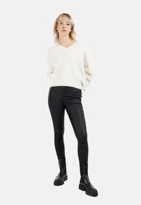 Pulover alb cu textură, cu decolteu în V și tiv din tricot, combinat cu pantaloni negri, ajustați și botine negre cu tălpi groase.