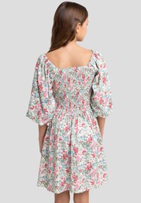 Blomstret kjole med firkantet halsudskæring, korte puffærmer og smock-bodice. Farverne inkluderer rød, pink, blå og grøn på en lys baggrund.