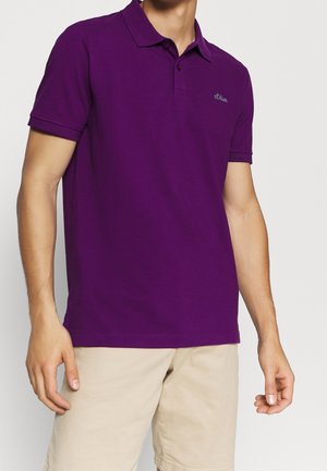 Polo de color púrpura con cuello, manga corta y logotipo bordado en el pecho; combinado con pantalones cortos beige claros. Textura suave.