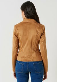 Hnědá umělá sukně s přiléhavým střihem, hladkou texturou a strukturovaným límcem. Obsahuje přiléhavé rukávy a mírně zkrácený lem.