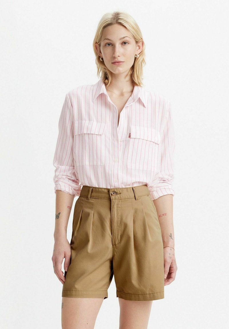 Camicia a maniche lunghe rosa chiaro con strisce bianche e due taschini sul petto, abbinata a pantaloni corti beige a vita alta con chiusura a bottone e pieghe.
