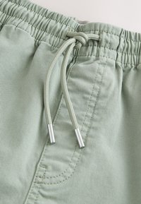 Shorts vert clair en coton avec une ceinture élastique, un cordon de serrage ajustable et des accents en métal argenté. Comprend une poche latérale.