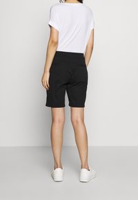 Černé šortky s jednoduchým designem, délka do polovin stehna, s bočními kapsami a hladkou texturou, kombinované s bílými teniskami a jednobarevným bílým topem.