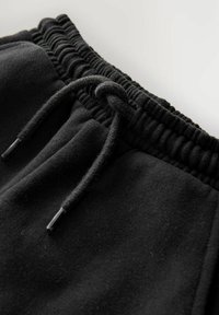 Mustat fleece-treenihousut, joissa on joustava vyötärö ja säädettävä naru metallipäillä, näyttävät pehmeältä pinnalta ja saumat.
