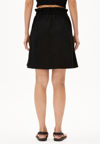 Schwarzer Rock aus leichtem Stoff, mit einem elastischen, gerafften Taillenbund und einem ausgestellten Schnitt, dessen Saum über der Mitte des Oberschenkels endet.