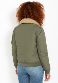 Giacca bomber verde oliva con colletto in pelliccia sintetica beige, polsini e orlo a coste. Materiale imbottito con una texture liscia, mostrata di spalle.