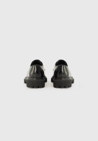 Chaussures en cuir verni noir avec une semelle épaisse noire et un bout arrondi. Présente une texture lisse et un design minimaliste. Vue arrière montrée.