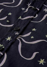 Sort stof med et svunget lysfarvet mønster og små stjerne-motiver, der har sorte knapper og en glat tekstur.