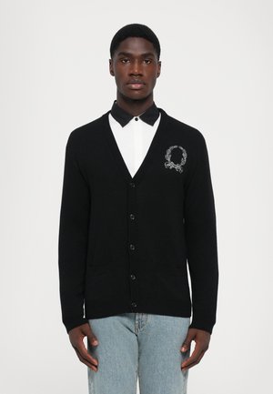 Schwarze Strickjacke mit V-Ausschnitt, fünf Knöpfen und zwei vorderen Taschen. Verziert mit einem weißen gestickten Kranzdesign auf der Brust.