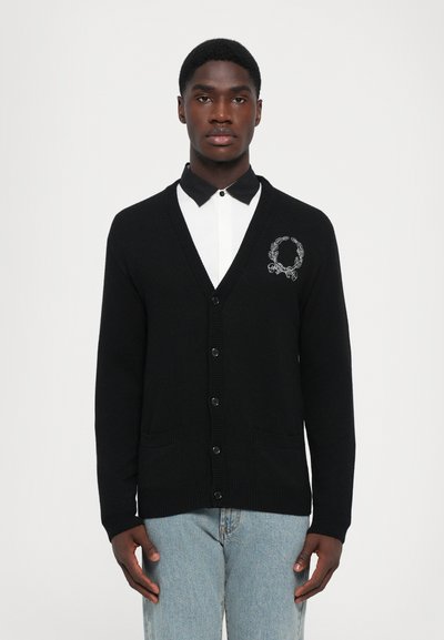 Cardigan noir avec un col en V, cinq boutons et deux poches avant. Présente un design de couronne brodé blanc sur la poitrine.