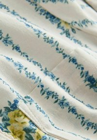 Tissu blanc avec des rayures florales bleues et un coin plié comportant un petit patch de fleurs jaunes et bleues.