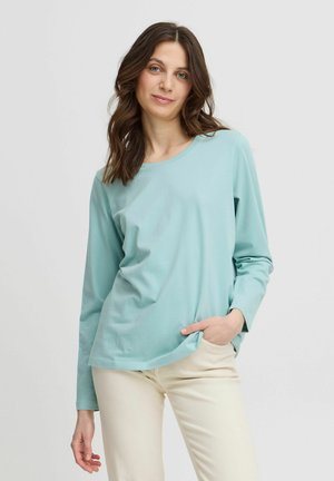 T-shirt azzurro chiaro a maniche lunghe con scollatura rotonda, realizzato in materiale morbido, abbinato a pantaloni beigi. Presenta una vestibilità ampia e una leggera texture.