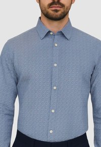 Hellblaues Hemd mit Knopfleiste, das ein dezentes geometrisches Muster aufweist, aus Baumwollmaterial gefertigt ist und Knopfmanschetten besitzt, mit klassischem Kragen und schlankem Schnitt.