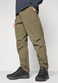 Calças cargo verde-azeitona com um acabamento texturizado, apresentando múltiplos bolsos e um corte descontraído, combinadas com sapatos de caminhada pretos.