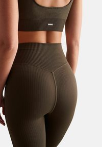 Un ensemble de brassière de sport côtelée vert olive et de leggings taille haute, présentant des lignes verticales texturées et un logo subtil dans le dos.