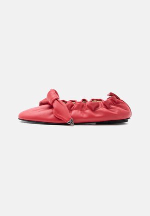 Red leather flat shoe with gathered elastic back and knotted bow detail on the front with a small metal triangle accent.